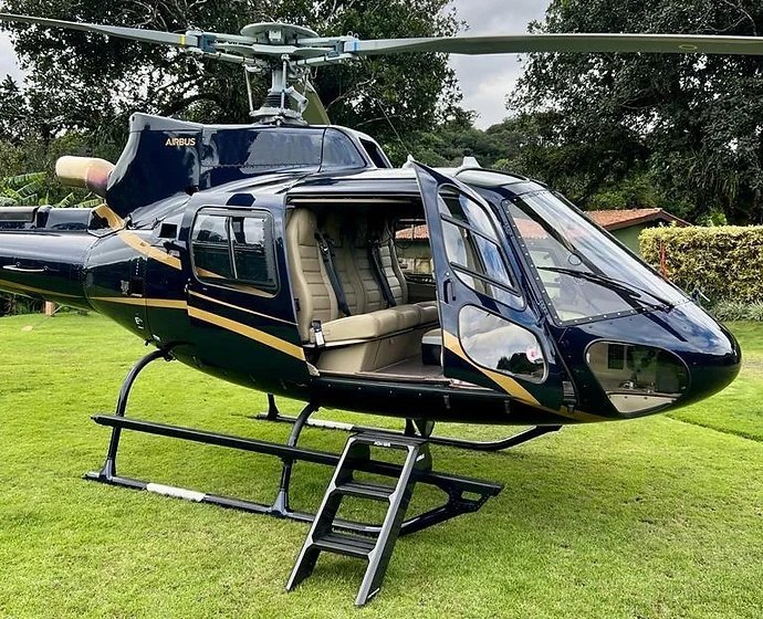 A black and gold Airbus H125 on a lawn with its cabin door open and boarding steps down